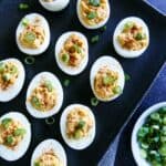Deviled eggs on a black tray with green onions, a delicious and healthy snack recipe.
