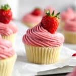 Gluten-free pink frosted cupcakes with strawberries on a baking sheet.