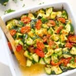 50 Easy Gluten Free Dinners featuring zucchini and tomatoes, served in a baking dish with a wooden spoon.