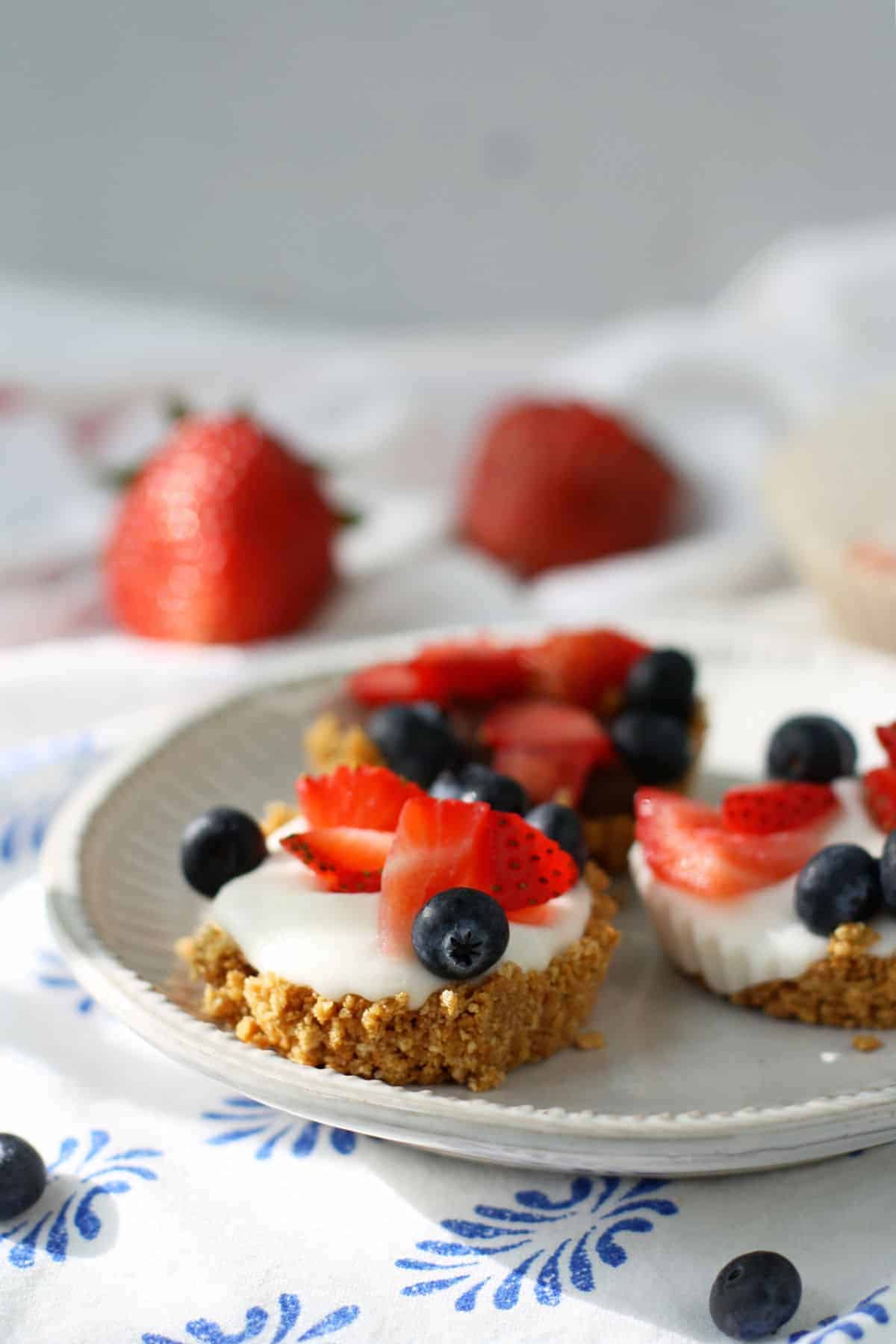 A plate of easy and gluten free berries and cream cheese tarts on a blue tablecloth.