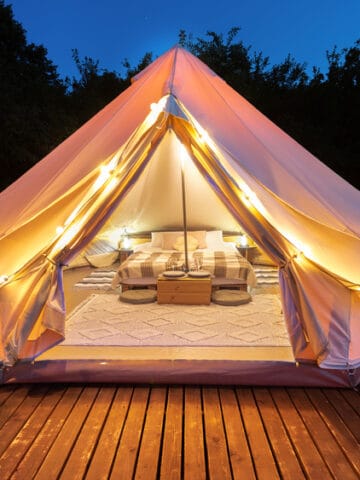 Tent interior and exterior with lamps and wooden chairs at glamping, forest around, night
