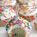 Gluten-free and dairy-free rainbow sprinkle cupcakes with a bite taken out of them.