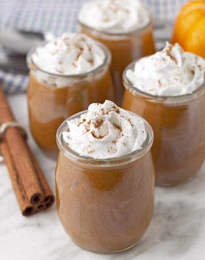 Easy pumpkin pie in jars with whipped cream and cinnamon sticks, a perfect gluten-free dessert option.