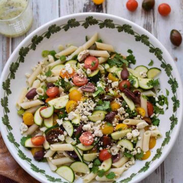A bowl of gluten-free pasta salad with tomatoes, cucumbers, and olives.