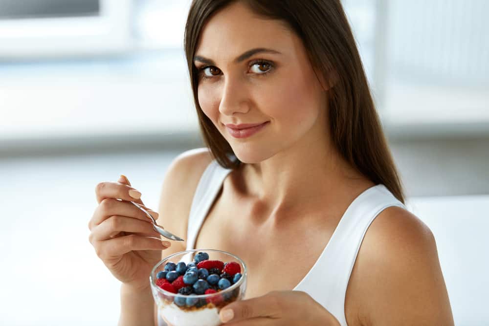 Healthy Eating Woman. Closeup Of Beautiful Happy Young Female Holding A Glass With Natural Yogurt, Delicious Berries And Crunchy Cereal In Morning. Breakfast, Diet Nutrition Concept. High Resolution