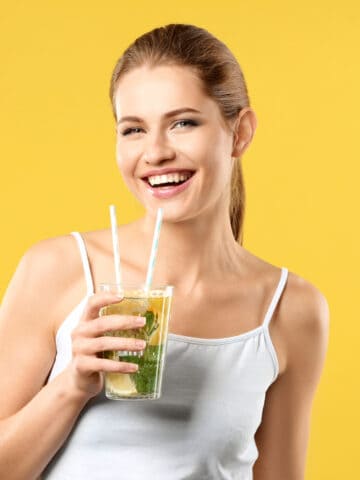 Beautiful young woman with glass of lemonade on color background