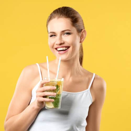 Beautiful young woman with glass of lemonade on color background