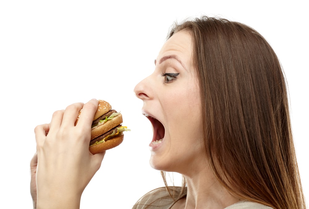Young caucasian woman preparing to bite a big burger, isolated on white background