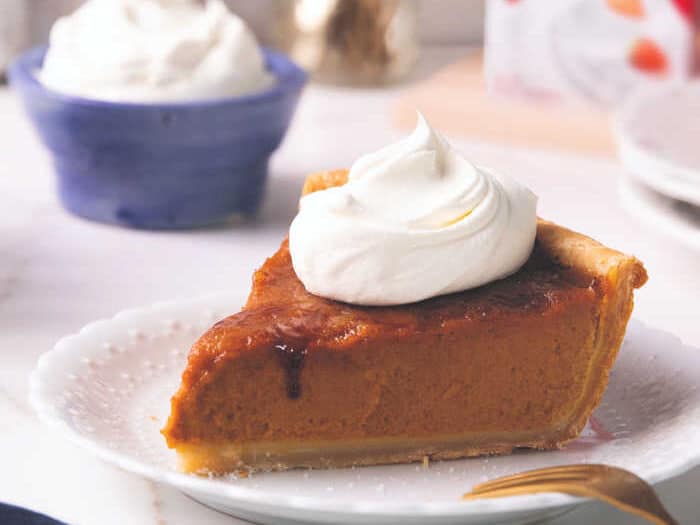 Slice of pumpkin pie on a white plate with whipped cream.