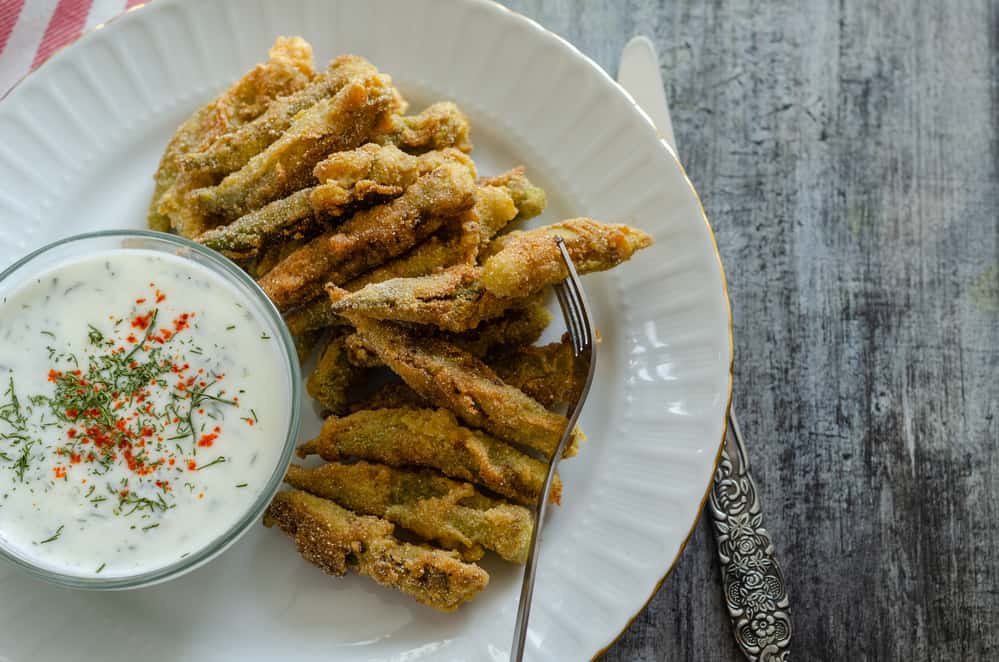 The crispy fried okra in container and spicy yogurt sauce on wooden table.