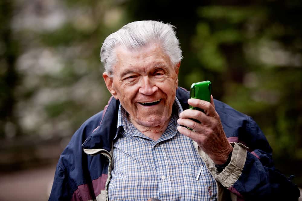 An old man laughing and smiling with a cell phone.
