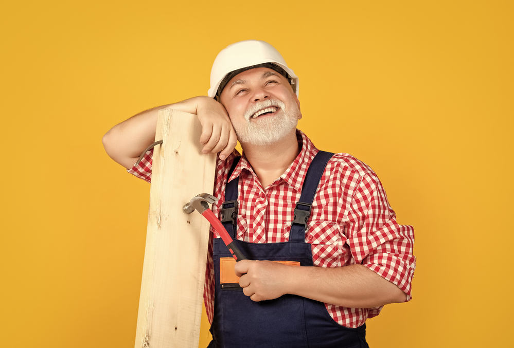 positive old aged man woodworker in helmet on yellow background.