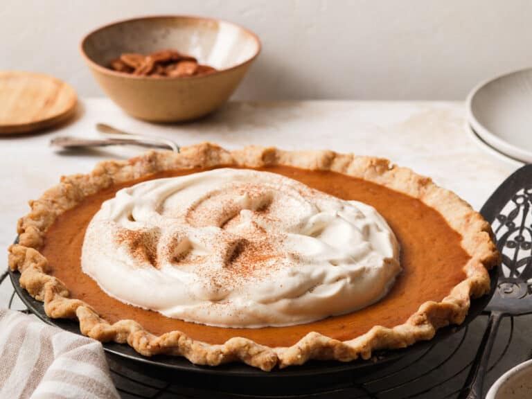 Pumpkin pie with whipped cream on a cooling rack.
