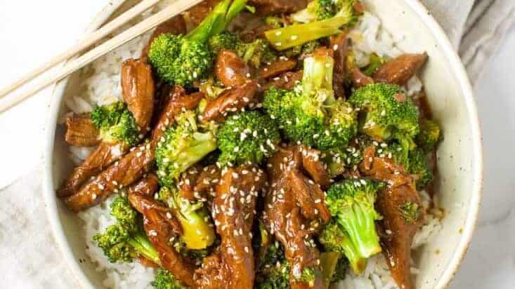 Beef and broccoli served over rice with chopsticks.