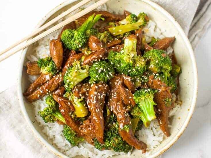 Beef and broccoli served over rice with chopsticks.