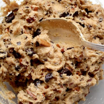 Raw cookie dough being mixed with chocolate chunks and chopped pecan nuts
