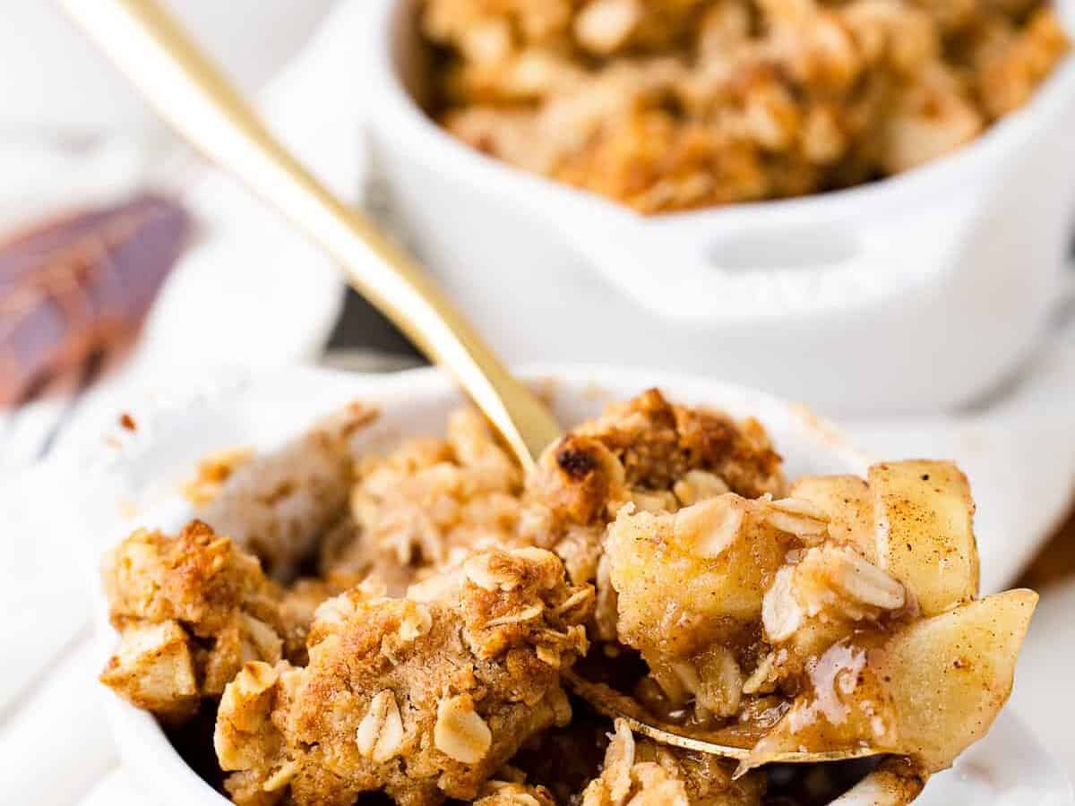 Apple crisp in a white bowl with a spoon.