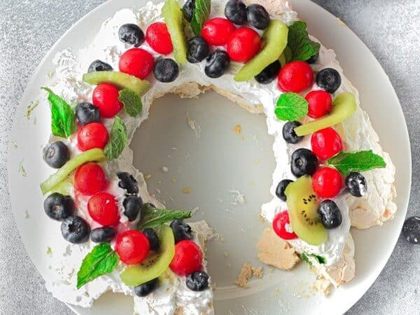 Pavlova with berries and mint on a white plate.