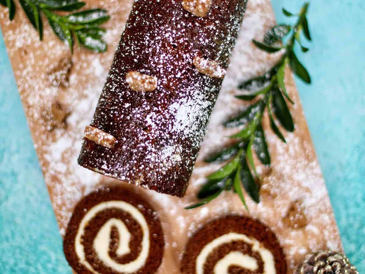 A christmas roll with powdered sugar and pine cones on a wooden cutting board.