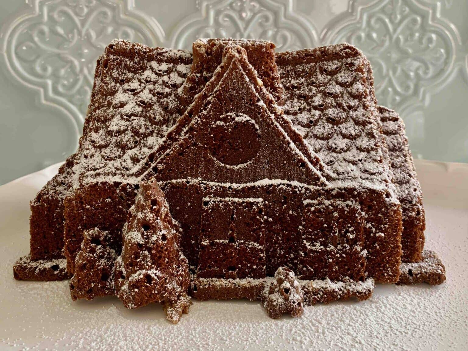 A gingerbread house on a plate with powdered sugar.