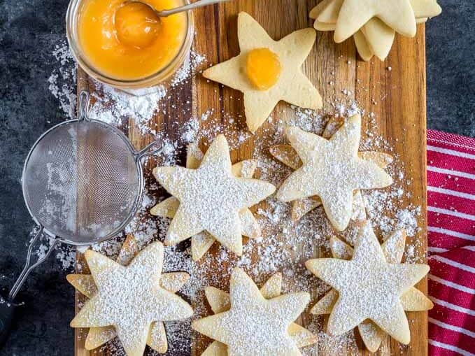 Star shaped cookies on a cutting board with powdered sugar.