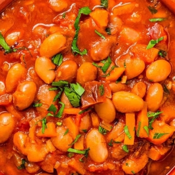 A bowl of white beans in tomato sauce, perfect for hearty soups with beans, placed elegantly on a table.