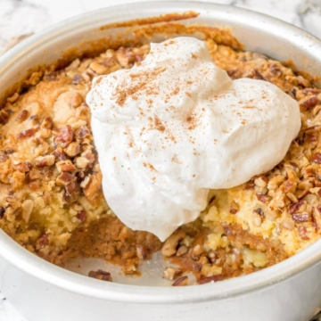 Pumpkin bread pudding in a pan served with whipped cream.
