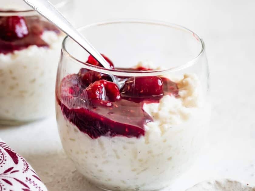 A glass of rice pudding with cherries in it.