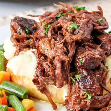 A plate of crockpot pulled pork with mashed potatoes and carrots, perfect for those who love hearty meat dishes.