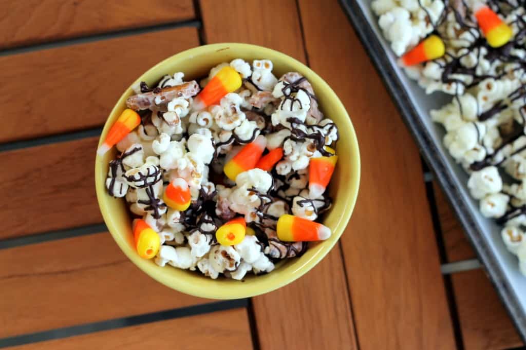 A bowl of popcorn with white chocolate drizzle and candy corn.