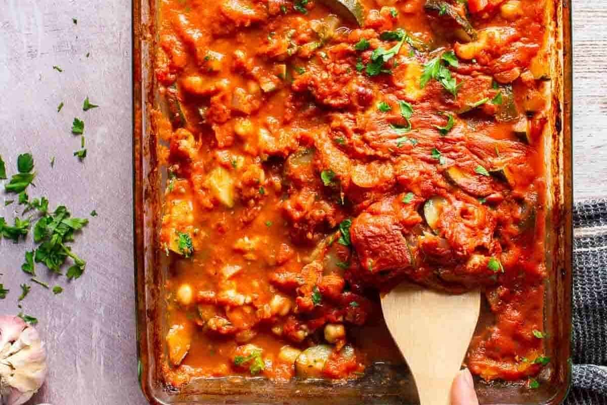 Mediterranean Vegetable Casserole with Chickpeas in a clear dish with wooden spoon.