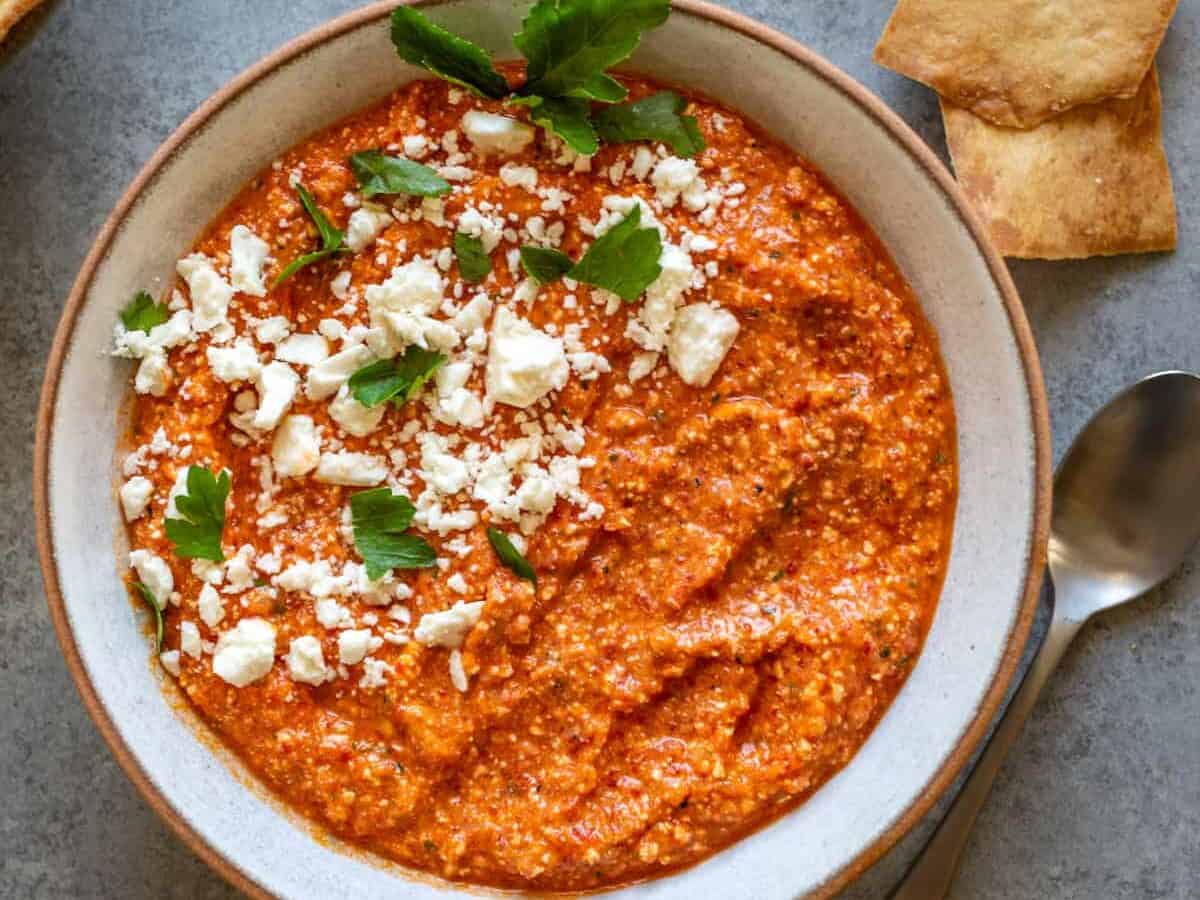 A bowl of roasted red pepper dip with feta cheese and tortilla chips.