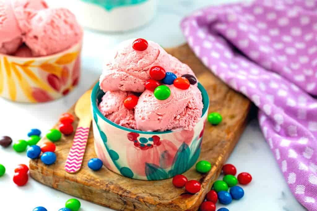 A bowl of pink ice cream with skittles candy on top.
