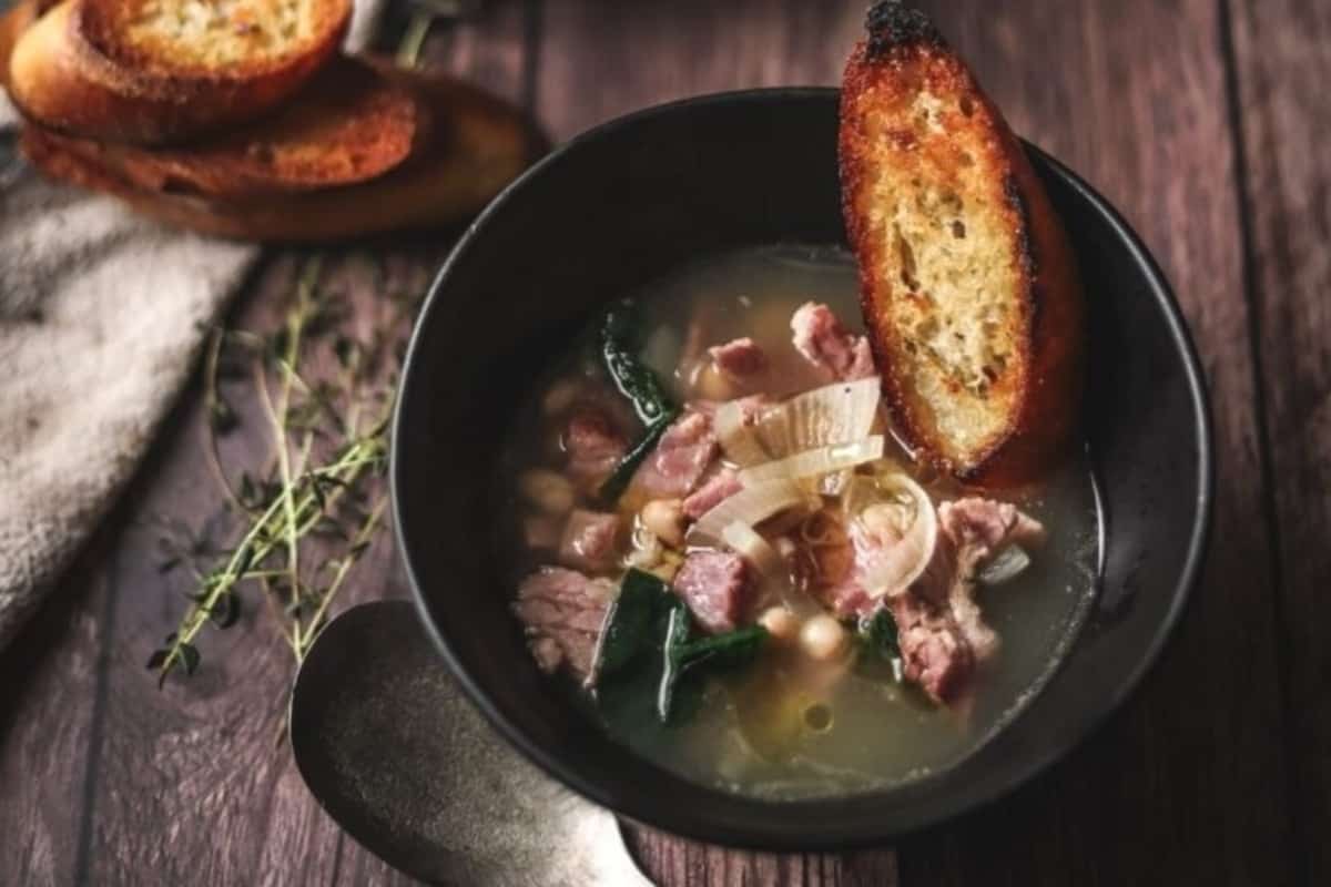 White bean ham soup with a piece of toast in a black bowl.