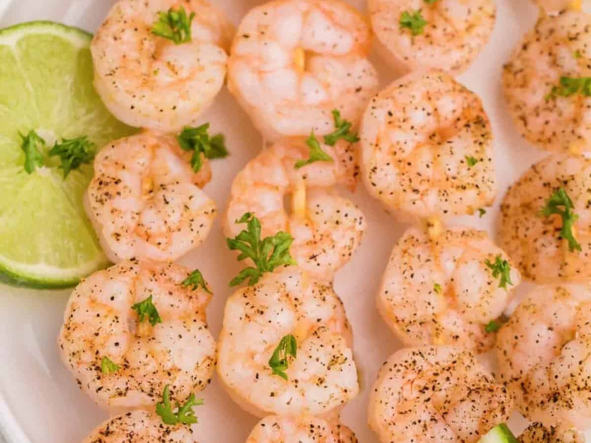 Shrimp skewers on a white plate with lime wedges.