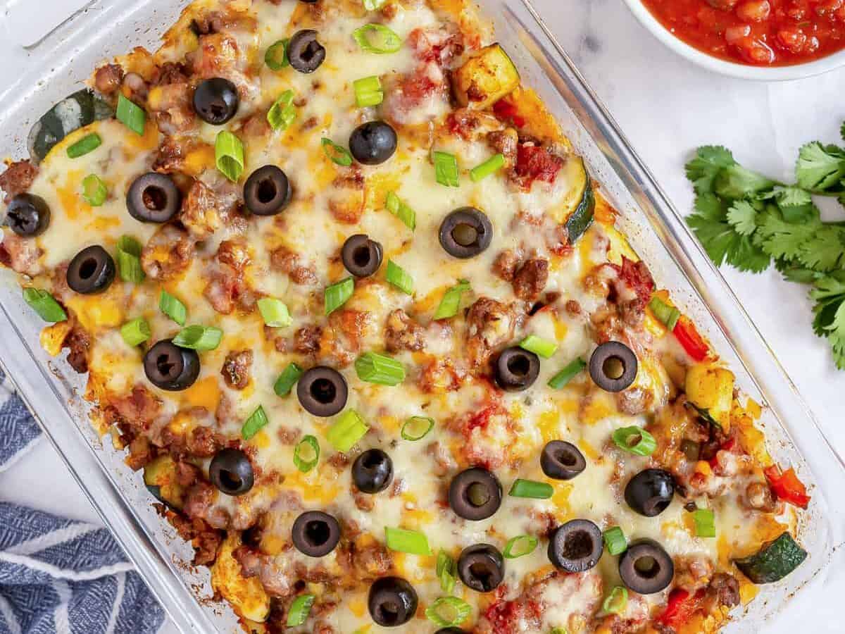 A casserole dish with taco casserole, topped with olives and green onions.