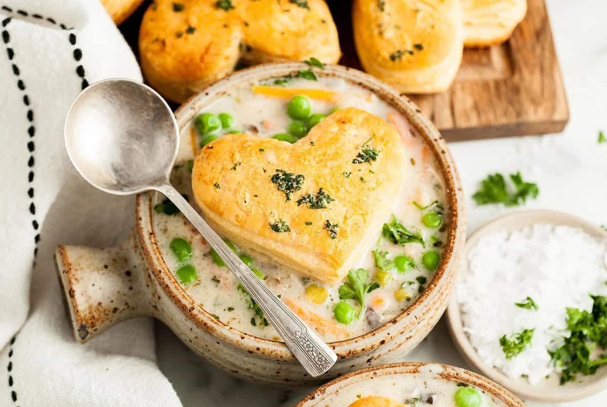 Chicken pot pie soup in a bowl with heart-shaped biscuit on top.