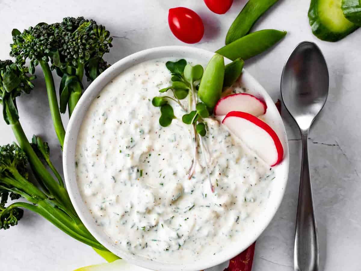 Ranch dip in a white bowl with vegetables.
