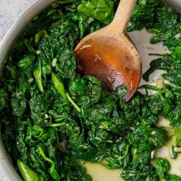 A delicious Thanksgiving side dish of spinach sautéed in a pan with a wooden spoon, perfect for enjoying with family.