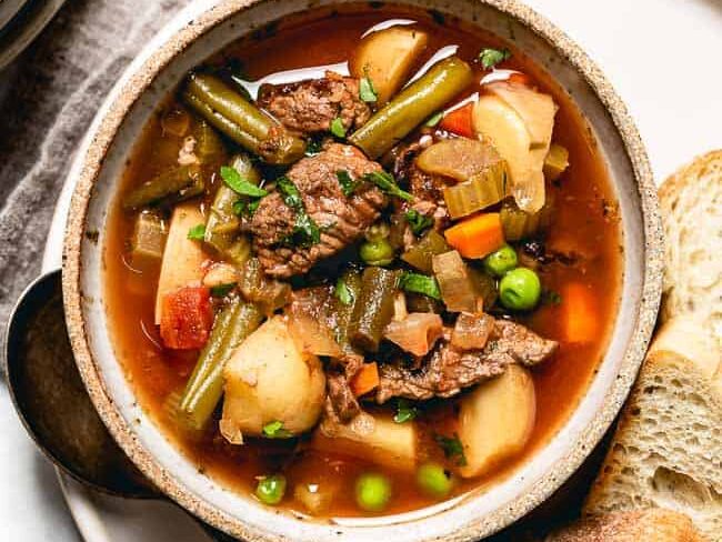 A bowl of Hearty Crockpot Vegetable Beef Soup with bread. 