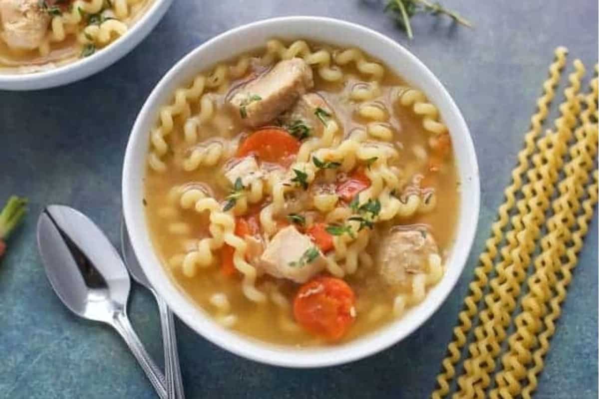 Chicken noodle soup with carrot slices.