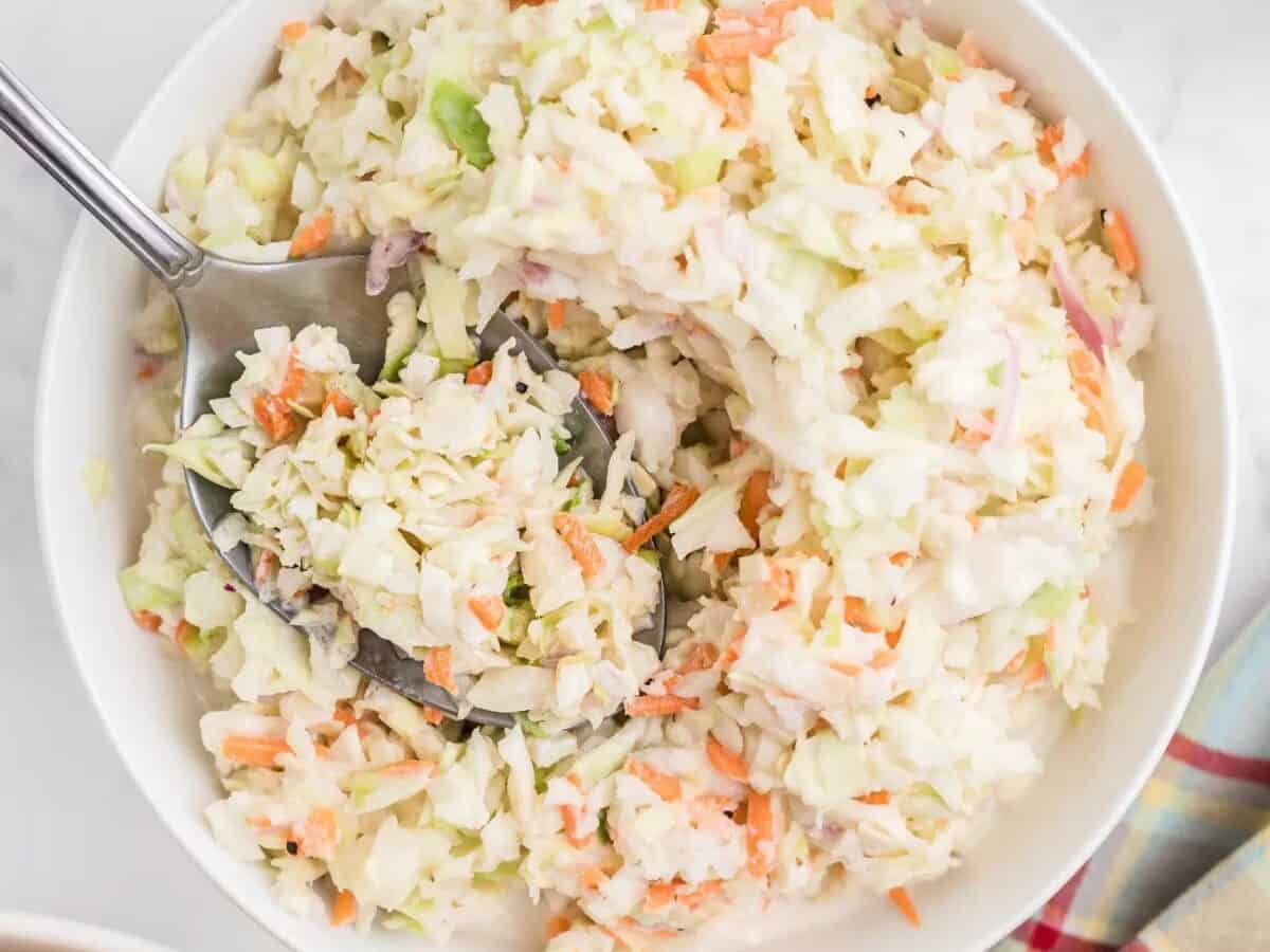 Coleslaw with a spoon in a white bowl.