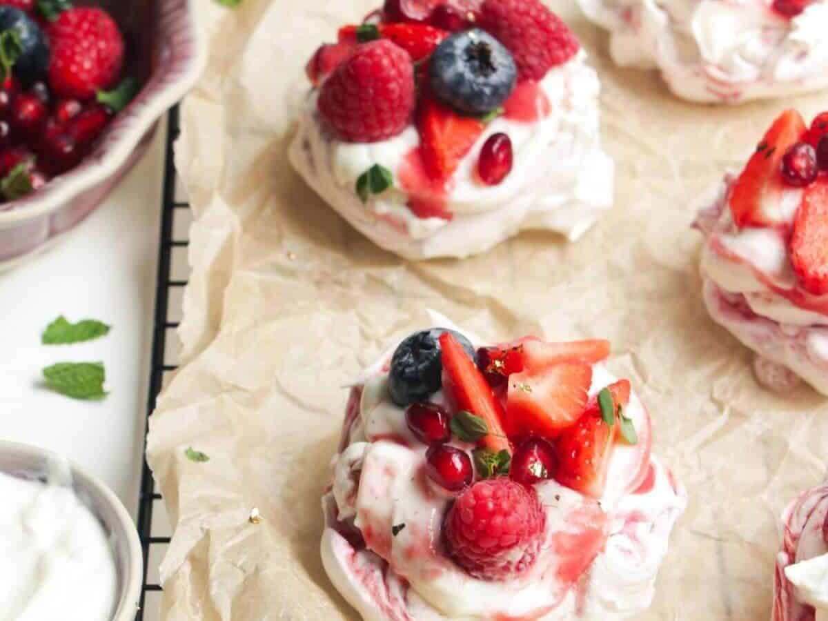 Mini Berry Ripple Cheesecake Pavlovas on a parchment paper.