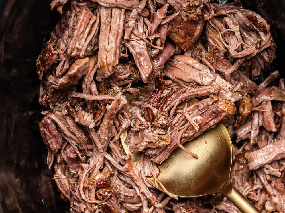Pulled beef in a dish with a serving spoon. 