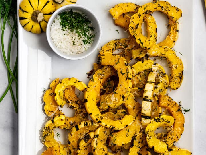 Roasted delicata squash on a white tray with herbs on side.