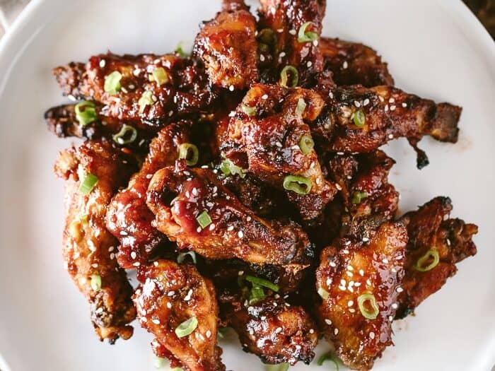 Pile of sticky chicken wings on a white plate.
