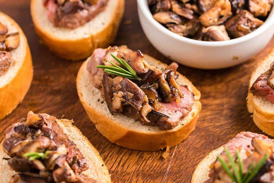 Steak and mushrooms on toast on a brown board.