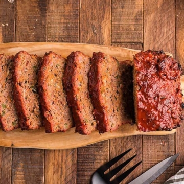 Delicious sliced meatloaf and corn on a wooden cutting board.