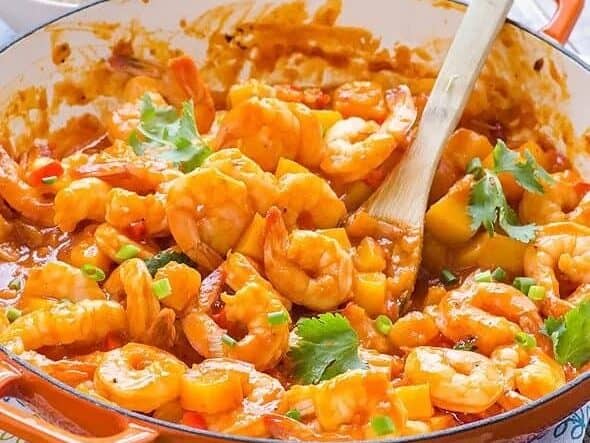 A pan full of shrimp in a sauce with a wooden spoon.