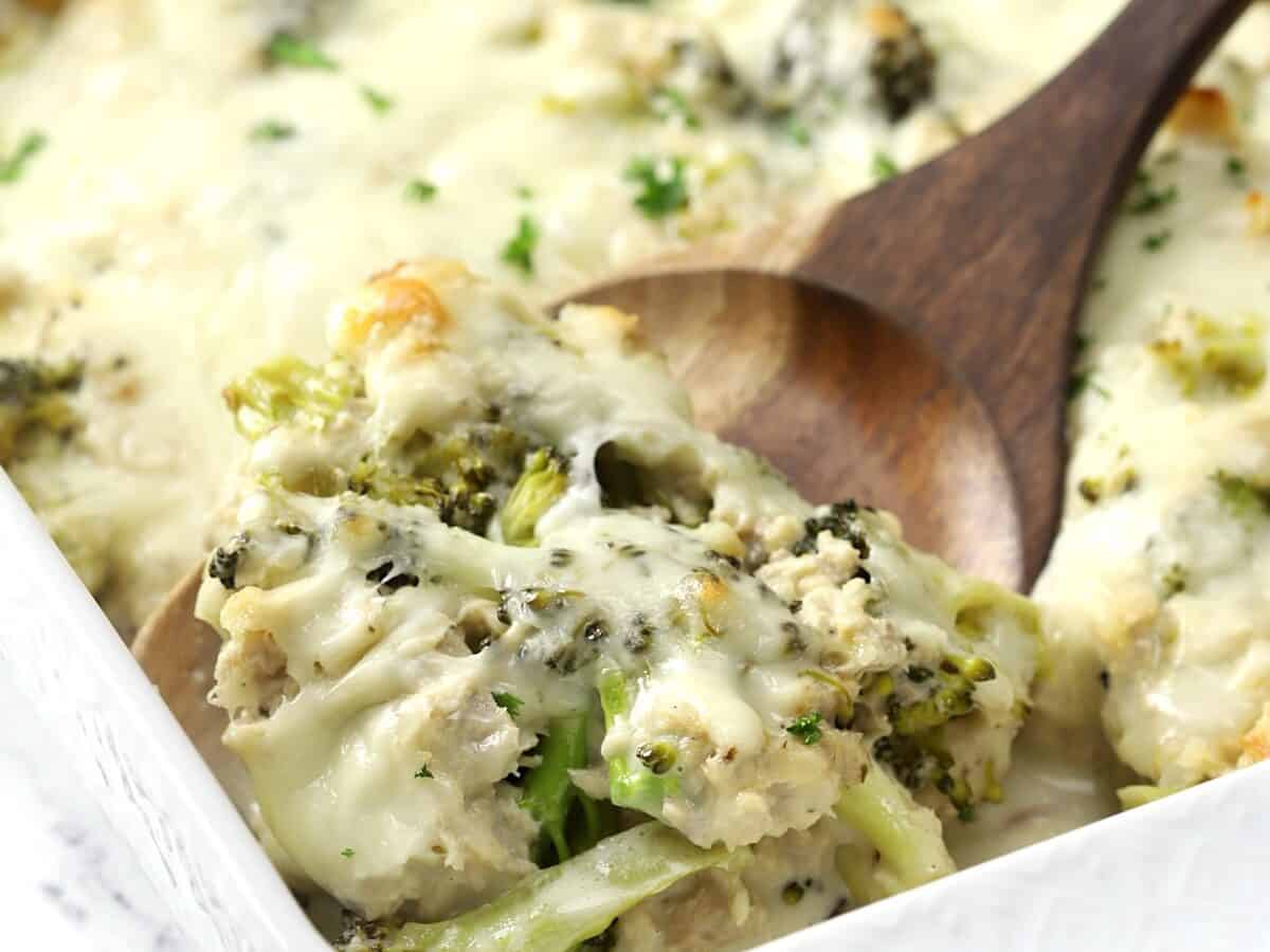 A casserole dish with tuna, broccoli and alfredo sauce with a serving spoon.